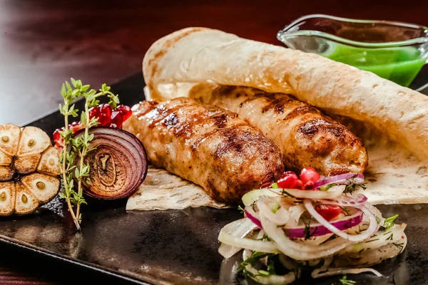 lulia Kebap sos ile siyah bir tabakta. Soğan, biberiye ve sarımsak dekorasyon