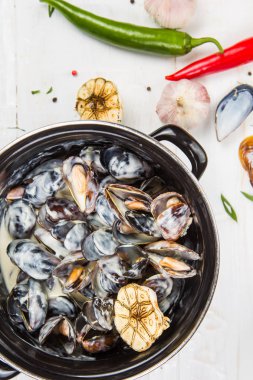sarımsak soslu midye. siyah bir tavada. Beyaz ahşap zemin üzerinde arka plan sebze ile dekore edilmiştir.