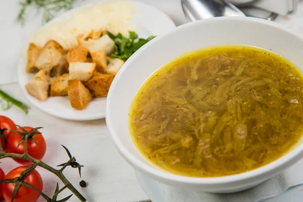 Луковый суп в белой тарелке с крекерами на белом деревянном фоне. Фон украшен овощами . — стоковое фото