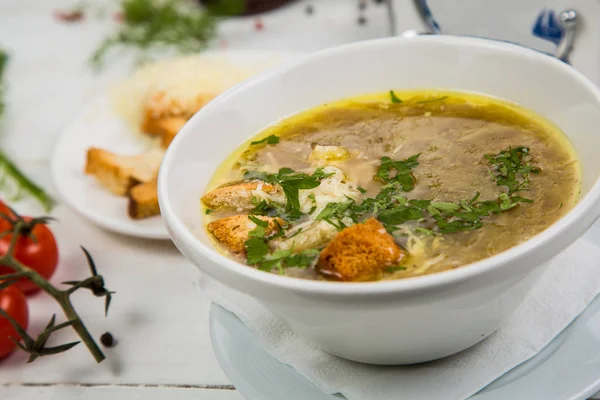 Zuppa di cipolle in un piatto bianco con cracker su uno sfondo di legno bianco. Lo sfondo è decorato con verdure . — Foto Stock