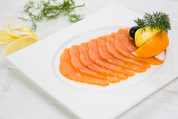marinated salmon with lemon and orange. decorate with herbs. on white wooden backfround