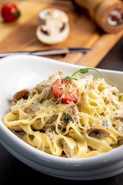 Mantar ve kızarmış tavuk jambon krem peynir soslu makarna fettuccine. Belgili tanımlık siyah geçmiş sebze ve bir kesme tahtası ile süslüdür