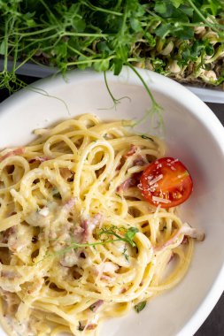 Makarna carbonara kiraz domates ile beyaz bir tabak içinde. Sebze ile dekore edilmiş siyah arka plan.
