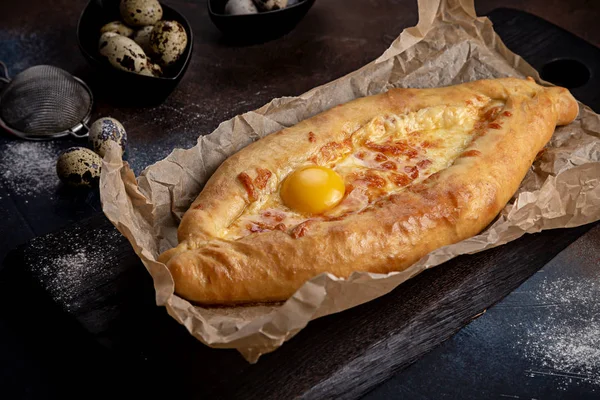 Ajarian Khachapuri geleneksel Gürcistan peynirli pastası ve üzerinde yumurtalar var. Bıldırcın yumurtalarıyla süslenmiş koyu renk bir arka plan.