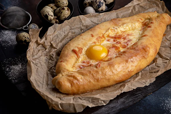 Ajarian Khachapuri geleneksel Gürcistan peynirli pastası ve üzerinde yumurtalar var. Bıldırcın yumurtalarıyla süslenmiş koyu renk bir arka plan.
