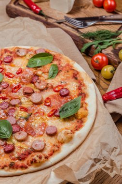 çeşitli sosis ve acı biber ile İtalyan pizza, arka plan ahşap bir arka plan üzerinde, sebze ile dekore edilmiştir