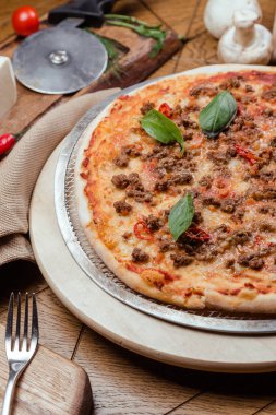Ahşap bir tahta üzerinde fesleğen ile Pizza Bolognese, arka plan ahşap sebze ve çatal ile dekore