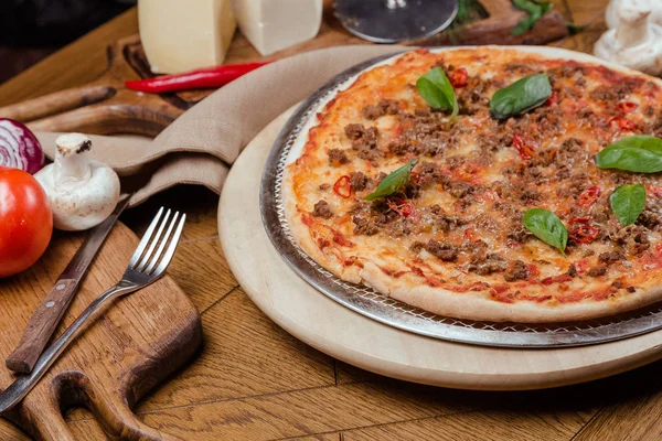 Ahşap bir tahta üzerinde fesleğen ile Pizza Bolognese, arka plan ahşap sebze ve çatal ile dekore