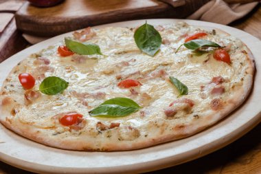 Tahtada fesleğenli pizza, sebze ve çatal bıçakla süslenmiş ahşap bir arka plan.