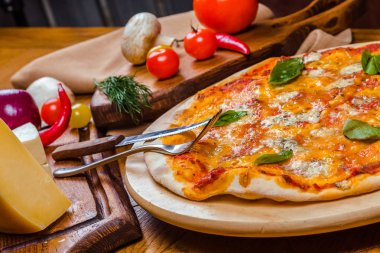 Ahşap bir tahta üzerinde fesleğen ile Pizza dört peynir, ahşap arka plan sebze ve çatal ile dekore