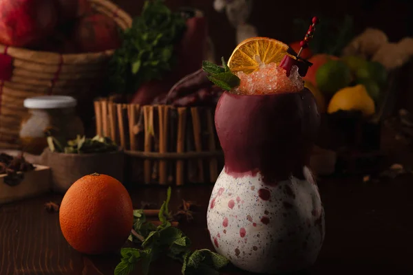 Oranje cocktail in een tiki glas op een houten ondergrond. Achtergrond versierd met fruit en kruiden. — Stockfoto