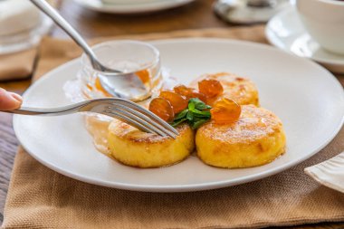 Reçelle kaplı kremalı kekler bıçakla kesilip çatala batırılıyor. Reçelli cheesecake ile kahvaltı. Arka planda bir fincan çay..