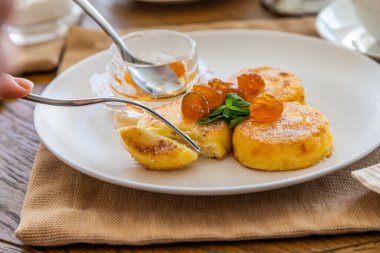 Reçelle kaplı kremalı kekler bıçakla kesilip çatala batırılıyor. Reçelli cheesecake ile kahvaltı. Arka planda bir fincan çay..