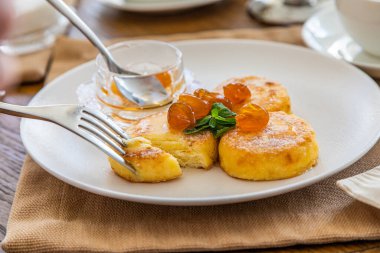 Reçelle kaplı kremalı kekler bıçakla kesilip çatala batırılıyor. Reçelli cheesecake ile kahvaltı. Arka planda bir fincan çay..