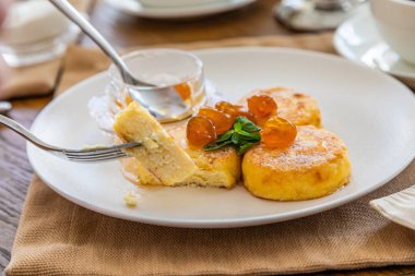 Reçelle kaplı kremalı kekler bıçakla kesilip çatala batırılıyor. Reçelli cheesecake ile kahvaltı. Arka planda bir fincan çay..