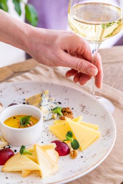 El bir bardak beyaz şarap alır. Peynir tabağı. Çeşitli peynirlerle dolu bir tabak. Atıştırmalıklar Peynirli bir bardak şarap..