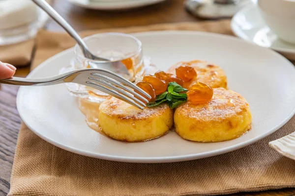 Reçelle kaplı kremalı kekler bıçakla kesilip çatala batırılıyor. Reçelli cheesecake ile kahvaltı. Arka planda bir fincan çay..