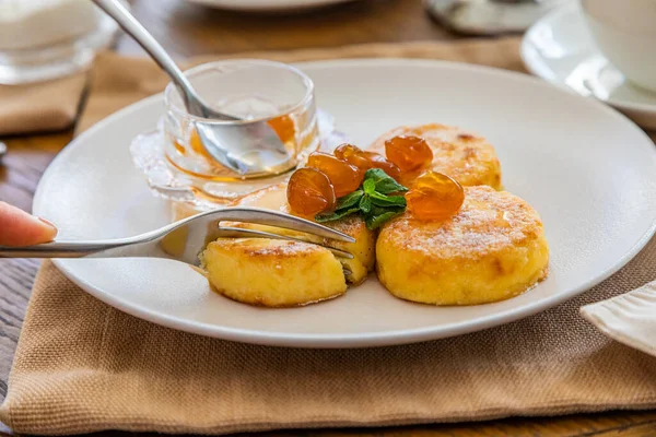 Reçelle kaplı kremalı kekler bıçakla kesilip çatala batırılıyor. Reçelli cheesecake ile kahvaltı. Arka planda bir fincan çay..