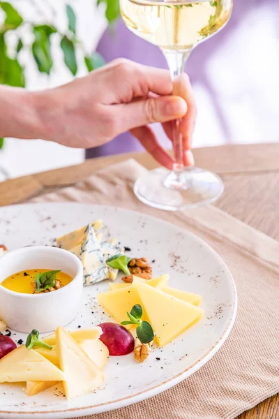 El bir bardak beyaz şarap alır. Peynir tabağı. Çeşitli peynirlerle dolu bir tabak. Atıştırmalıklar Peynirli bir bardak şarap..