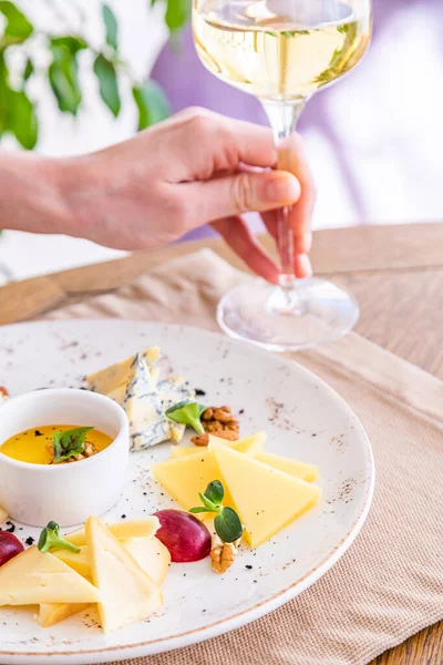 El bir bardak beyaz şarap alır. Peynir tabağı. Çeşitli peynirlerle dolu bir tabak. Atıştırmalıklar Peynirli bir bardak şarap..