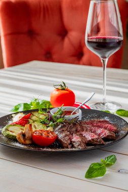 Orta pişmiş biftek ve ızgara sebze. Tabak domates sosu ve bir bardak kırmızı şarapla servis edilir. Tabak beyaz bir tabakta, doğal ışıkta.