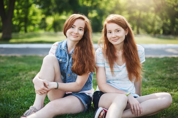 My sister is best friend. Good-looking two female with red hair and freckles, sitting on grass near university campus and chilling with boyfriends, smiling with cute expression while talking casually