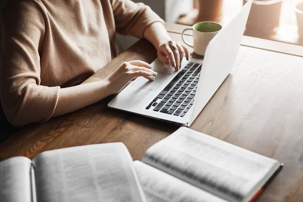 Bijgesneden schot van vrouw handen typen op toetsenbord terwijl u werkt in café met laptop, voorbereiden van materiaal voor Studiebegeleiding, controle informatie in boeken, messaging met collega te vragen advies via notitieboekje — Stockfoto