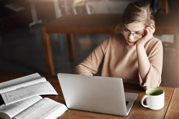 Girl concentrating on work, proofreading essays, leaning head on hand while sitting in cafe, working with laptop, drinking tea to focus and making notes, checking data in company account — Stock Photo, Image