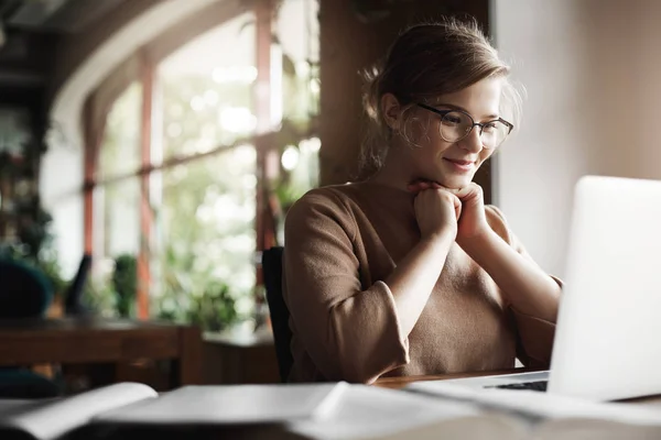 Girl being pleased with great job and positive result of work, sitting in quiet and cozy cafe, leaning head on hands and smiling broadly with satisfied expression at laptop, finishing project in time — Stock Photo, Image
