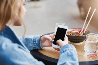 Masanın ayakta, ağ tarama, smarpthone üzerinden mesaj gönderme, Asya gıda sevme, soba çubukla yemek trendy kaygısız sarışın kadın gelecekteki gazeteci açık atış