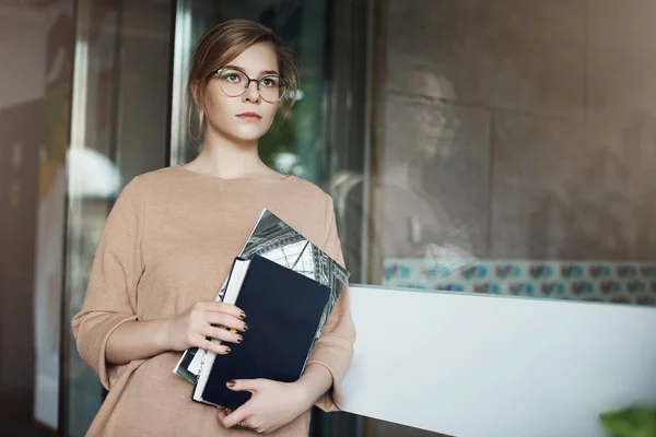 Girl walking down corridor on way to meeting room, gathering courage to make speech in front of business partners. Focused serious-looking attractive female, holding books and notebooks, looking aside — Stock Photo, Image