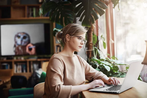 Good-looking successful fashion blogger writing new essay on laptop while sitting in cafe and waiting for coffee, looking at screen while browsing in internet, using web to create new content — Stock Photo, Image