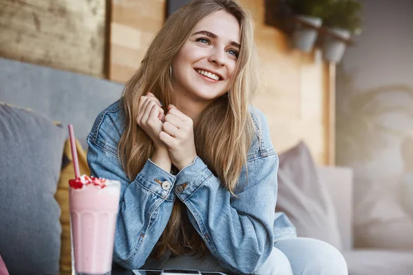 Wanita mudah jatuh cinta, melihat pria tampan berjalan di jalan. Portrait of tender touched atraky dreamy girl with fair hair in denim jacket, sitting in cafe and drink milkshake, smile — Stok Foto