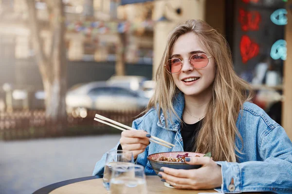 Dívka myšlení, co odpovědět, vyjádření výroku o chuť asijských potravin, opíraje se na stole stála před restaurací, zírající zasněný stranou, držení hůlek a bowk s ramen — Stock fotografie