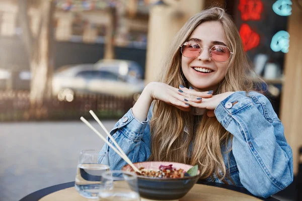 Městská žena rád velkoměsta, zíral na auta jít koupit při posezení v asijské restauraci, opřel se o stůl a radostně usmívá, soba jíst hůlkami, usmíval se a díval se stranou pobavilo — Stock fotografie