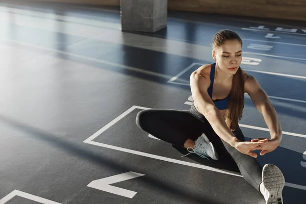 Focused woman athlete in sportswear sporty bra sitting gym floor stretching leg preparing muscles and biceps for working-out, pilates. Active young aerobics instructor practicing exercises — Stock Photo, Image