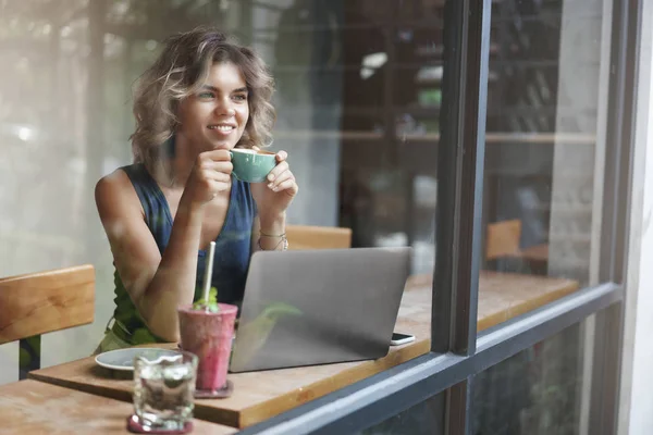 Aantrekkelijke stijlvolle vrouwelijke ondernemer werkt buiten kantoor Sit café kijk buiten venster voorbijgangers dromerige glimlachend houden kopje koffie geniet van momentum werken laptop voorbereiden project — Stockfoto
