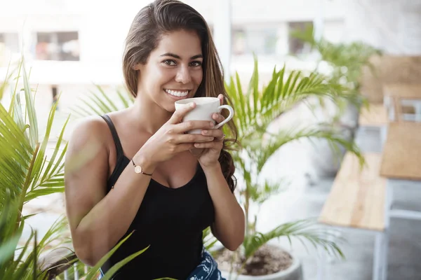 Ale první káva. Okouzlující vyčiněná žena si vychutnávat chutnou čajovou šálku s radostným úsměvem, začíná ráno s krásnou scenérií stojící na balkóně u rostlin a šťastně se směje — Stock fotografie