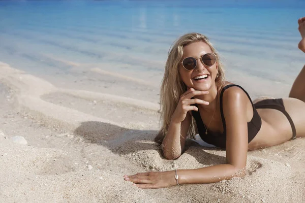 Woman brighten up beach white delighted smile. Attractive female tourist lie sandy beach ocean shore touch water feet wear black bikini wanna swim happily laughing look camera, relaxing — Stock Photo, Image