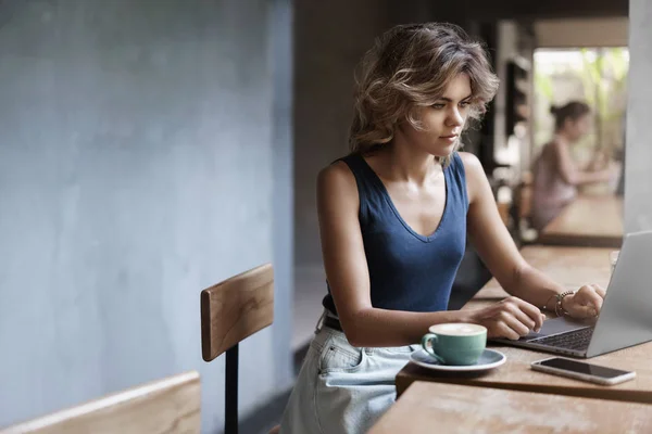 Attractive blond girl freelancer working laptop taking notes notebook sit alone cafe near window drink coffee, professional writer make post online blog, prepare files business meeting after lunch