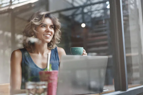 Karizmatikus bájos európai szőke göndör hajú sikeres nő inni kávét élvezni ebéd Sit Café ablak bár Nézd meg kívülről örömmel íz kávé tart csésze használata laptop, kutatása, dolgozó szabadúszó — Stock Fotó