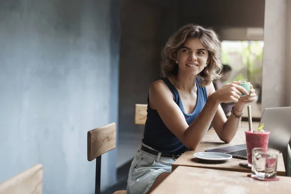 Dreamy menarik perhatian gadis pirang Kaukasia gaya rambut pendek berbalik tersenyum senang menikmati lezat cangkir smoothie kerja di luar kantor menggunakan laptop mempersiapkan tugas-tugas digital, belajar kafe duduk — Stok Foto