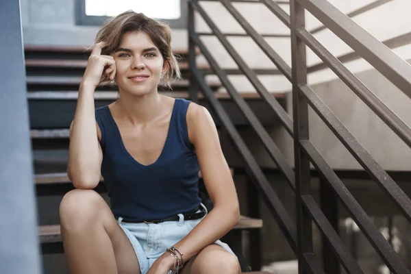 Attractive blond european young girl student sit alone outdoors stairs look camera talking friend resting after lesson university walking campus, relaxing enjoy summer warm weather, wear shorts — Stock Photo, Image