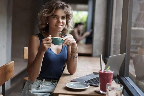 Attraente sicuro di successo imprenditore donna sedersi caffè vicino alla finestra di lavoro portatile bere caffè tenere tazza sorridente felicemente rilassato fotocamera studiando lo spazio di co-working, preparare il progetto online — Foto Stock