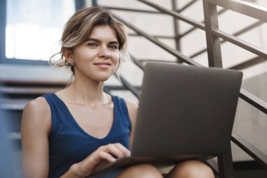 Şık iyi görünümlü mutlu genç kadın öğrenci hazırlamak üniversite presintation yalnız merdiven oturmak Hold laptop diz bakmak kamera memnun serbest çalışma gülümseyen, kurşun vanlife yaşam tarzı