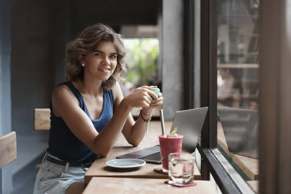 Charmante europäische blond gelockte Unternehmerin sitzen Café Fensterbar verwenden Laptop Kaffee trinken Pause arbeiten freiberuflich bereiten Universitätsprojekt, digitales Nomaden-Konzept — Stockfoto
