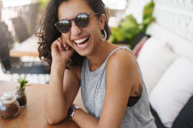 Yakın çekim neşeli mutlu samimi bronzlaşmalı kadın güneş gözlüğü yaz tank-top gülme sevinçle rahatlatıcı konuşma kız arkadaşı kafe veranda sehpa bekleme düzeni tatil gezisi zevk giymek
