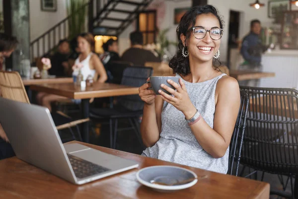 Meisje nemen moment ontspannen. Gelukkige vrouw krullend kort kapsel rusten werken laptop Sit café binnenshuis mager rotan stoel overweegt zomer uitzicht buiten venster glimlachend Hold Cup cappuccino nemen pauze — Stockfoto