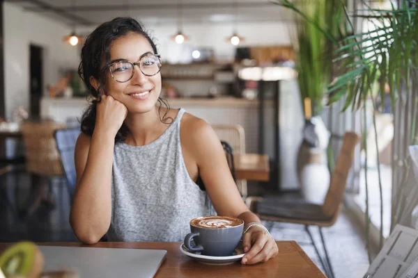 Rilassato attraente donna magra braccio inclinazione testa carino sorridente fotocamera sedersi caffè vicino alla finestra chiuso computer portatile finito lavoro godere di bella conversazione amichevole bere cappuccino in attesa fidanzato vicino all'ufficio — Foto Stock