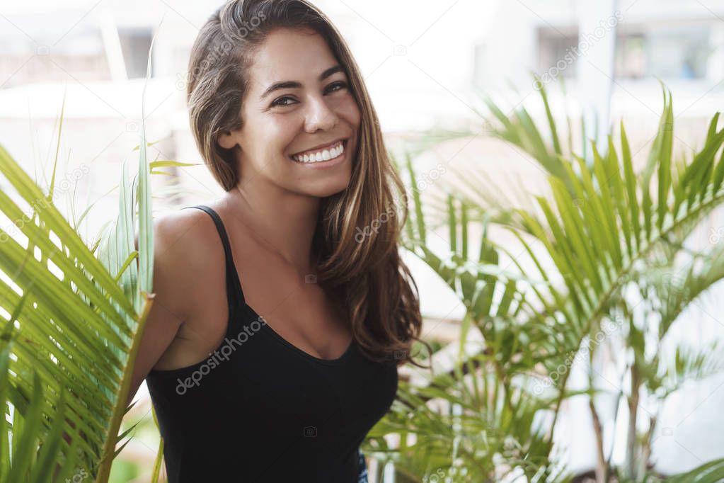 Carefree lovely tanned young woman standing balcony near green plant smiling laughing out loud look adorable grin camera talking casually coworker veranda, enjoy perfect sunny summer days